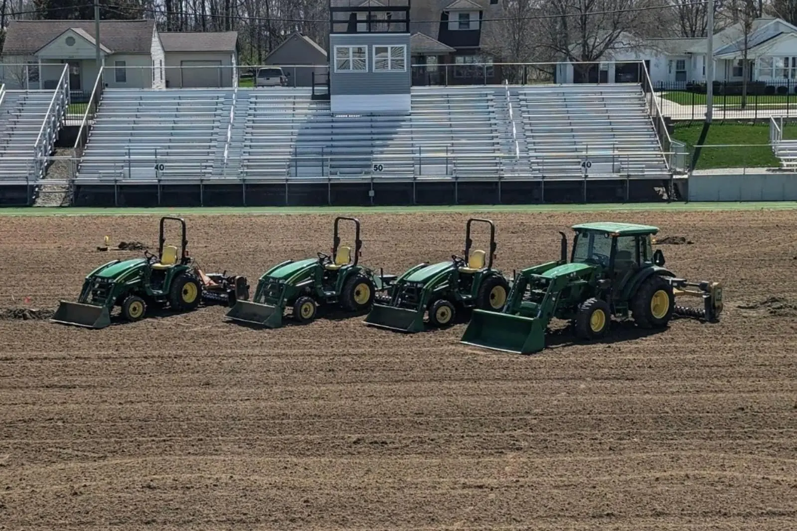 Four tractors lined up on a freshly tilled athletic field before grading, serving Dayton, OH